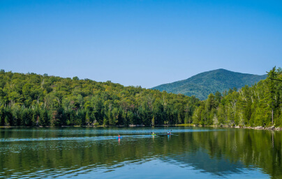 kayakers on calm summer lake with Adirondack mountains in distance