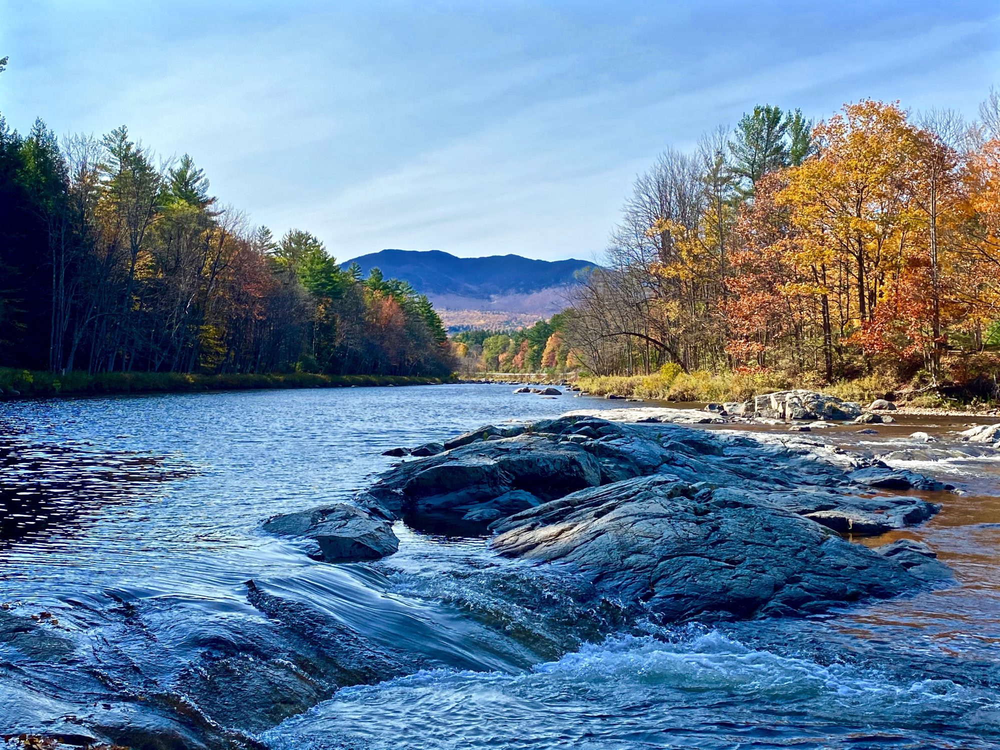 water flowing in Adirondack river with fall trees and mountains in distance